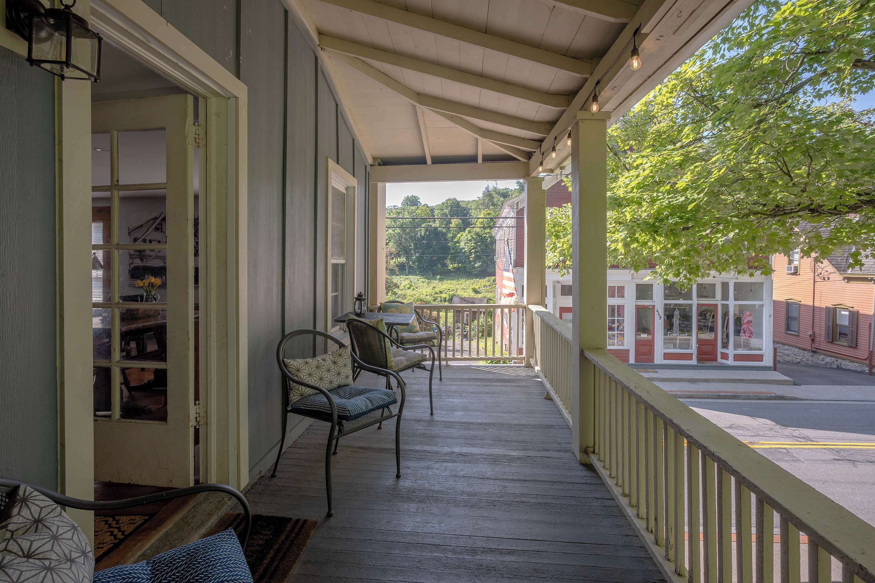 A porch with a table and chairs, a view of a street, and a building with a sign.