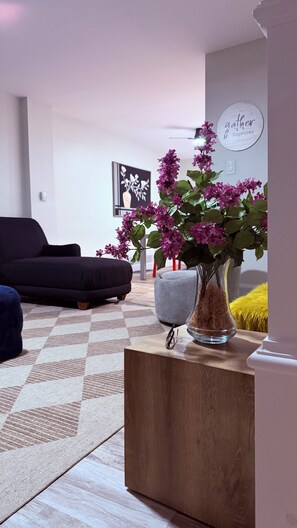 Ein Wohnzimmer mit einer Couch, einem Couchtisch mit Blumenvase, einem gerahmten Bild an der Wand und einem Schild mit der Aufschrift 'Gather Together'.