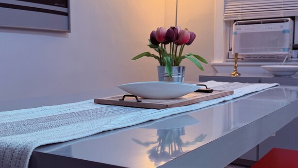 A modern dining area with a long table, a vase of flowers, a lamp, and a window with blinds. - Fantastic 3-bedroom house with AC in charming Camden (Camden)