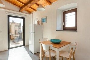 A kitchen with a white refrigerator, a wooden table with a teal bowl, white chairs, and a window with a brown frame. - Steinmelker House - Seneghe (Seneghe)