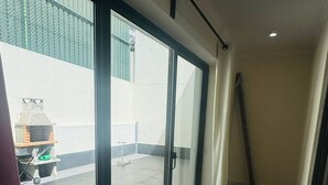 A room with a large window, a ceiling-mounted light fixture, and a view of an outdoor area with a fence and a grill. - Cozy 2-bedroom Apartment in Pontinha, Portugal (Amadora)