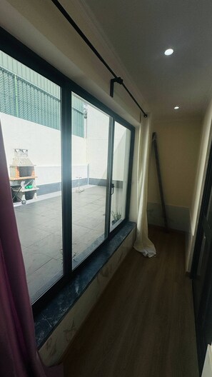 A room with a large window, a ceiling-mounted light fixture, and a view of an outdoor area with a fence and a grill. - Cozy 2-bedroom Apartment in Pontinha, Portugal (Amadora)