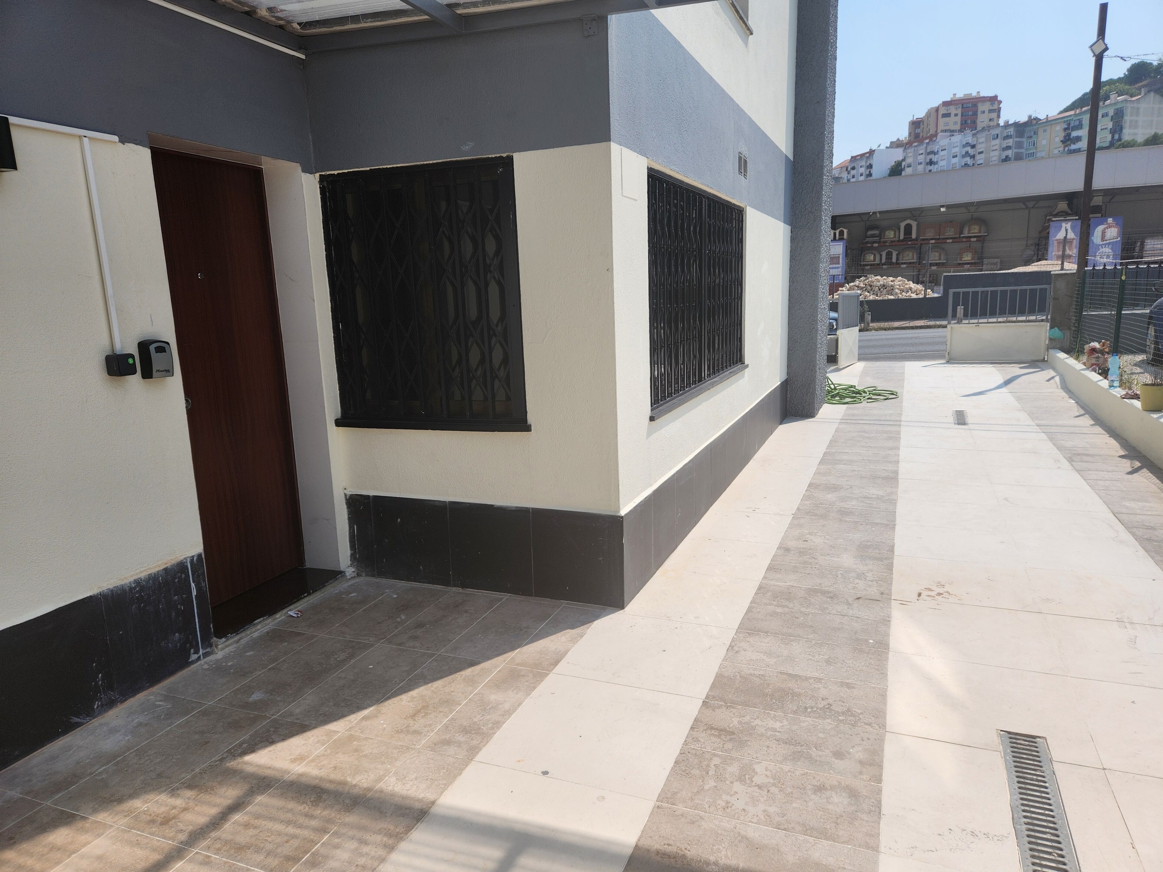 A building with a gated entrance, a tiled pathway, and a visible drainage grate.
