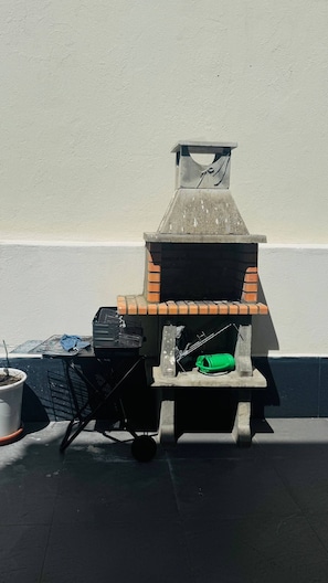 Een barbecue met schoorsteen, een zwarte grill en een groene tas op een betegeld terras.
