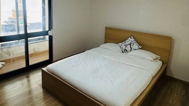 A bedroom with a wooden bed, a window, and a ceiling light. - Cozy 2-bedroom Apartment in Pontinha, Portugal (Amadora)