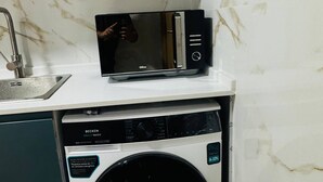 A compact kitchen with a microwave on a white countertop, a sink, and a dishwasher with a BoostWash label. - Cozy 2-bedroom Apartment in Pontinha, Portugal (Amadora)