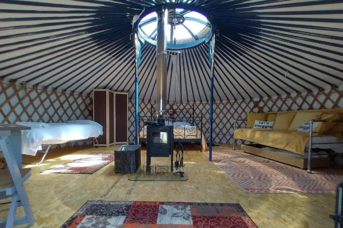 Eine Jurte mit Zentralheizung, einem Bett mit gelber Decke, einer Couch und einem gemusterten Teppich.