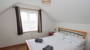 Et soveværelse med en seng, et sengebord, en lampe, et vindue med gardiner og en radiator.