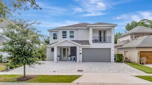 A modern two-story vacation home with a welcoming front entrance and covered balcony, set in a peaceful residential neighborhood with mature trees and landscaped grounds. - Reunion Resort: 8-Bed Villa, Arcade, Theater, Pool (Kissimmee)