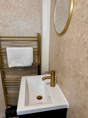 A bathroom with a gold towel rack, a white sink with a gold faucet, and a round mirror on the wall.