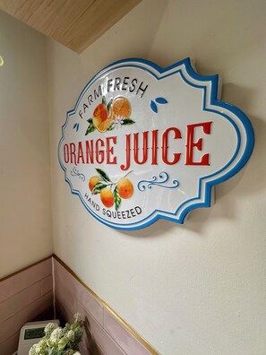 A wall sign with 'FARM FRESH ORANGE JUICE' and 'HAND SQUEEZED' text, surrounded by fruit illustrations.