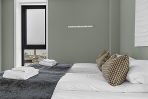 A hotel room with a bed, a window with a city view, a scale on the wall, and towels on the bed. - The View - City center apartment with spectacular views (Tromsø)