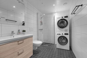 A modern bathroom with a toilet, sink, mirror, shower, and a stacked washer and dryer. - The View - City center apartment with spectacular views (Tromsø)