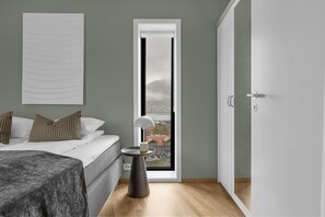 A bedroom with a bed, bedside table, lamp, and a view through a window. - The View - City center apartment with spectacular views (Tromsø)