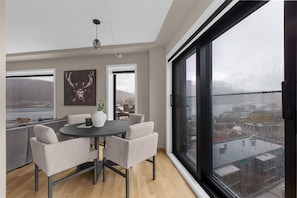 A modern dining area with a round table, chairs, and a city view through large windows. - The View - City center apartment with spectacular views (Tromsø)