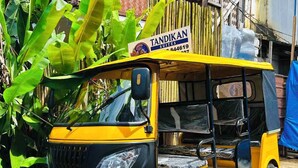 Un auto-rickshaw amarillo estacionado frente a un edificio con un letrero que dice 'TANDIKAN SUITES'.