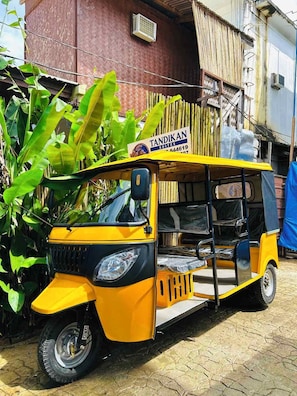 Ein gelbes Auto-Rikscha vor einem Gebäude mit dem Schild 'TANDIKAN SUITES'.