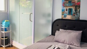 Un dormitorio con cama, armario de puertas de cristal, un cuadro en la pared y una mesita con un recipiente azul.