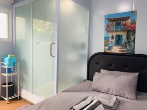 Un dormitorio con cama, armario de puertas de cristal, un cuadro en la pared y una mesita con un recipiente azul.