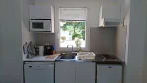 Eine kleine Küche mit Mikrowelle, Spüle und einem Fenster mit Jalousien.