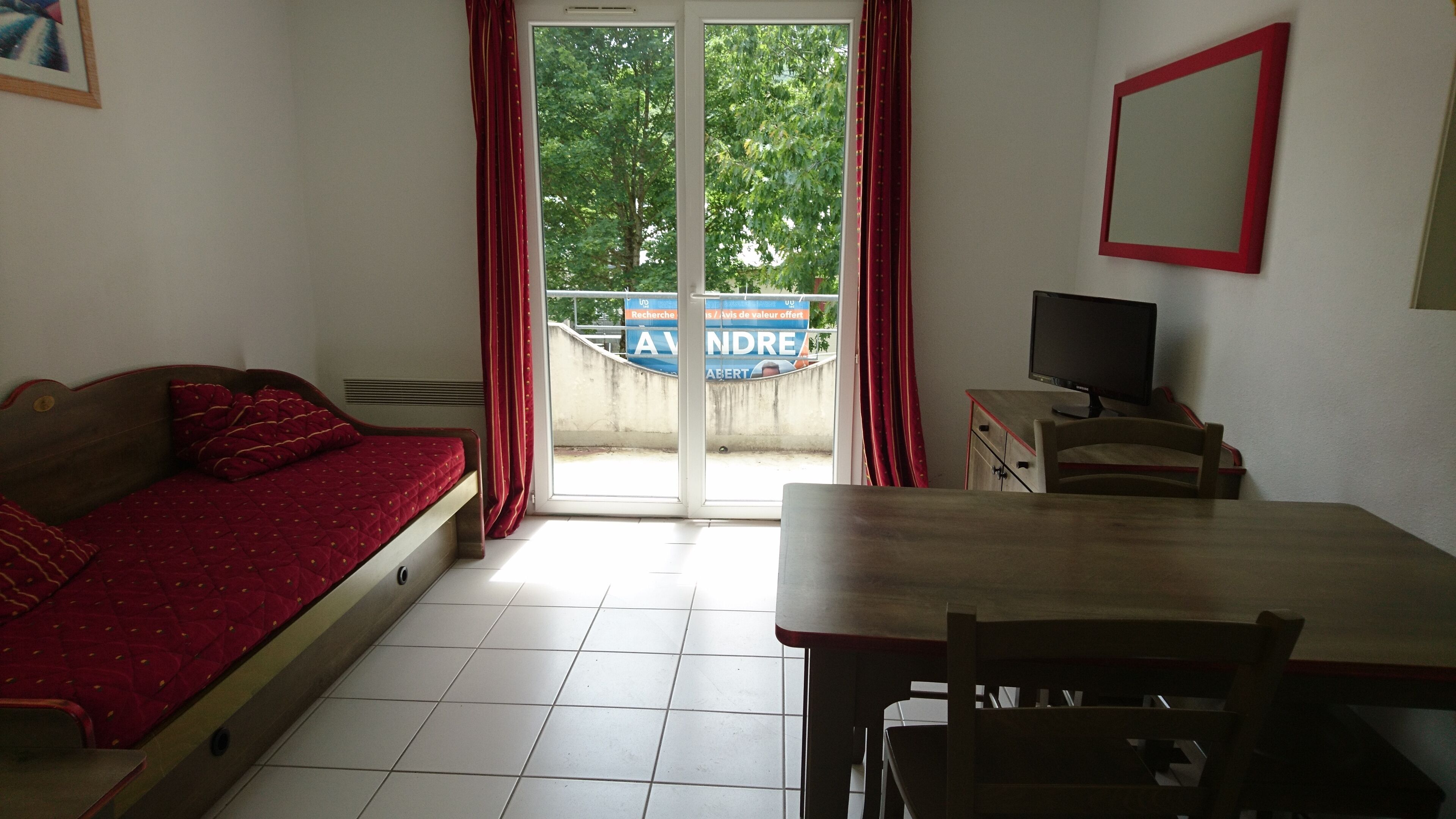 Una habitación con cama, escritorio, silla, televisor y puerta corrediza de vidrio que da a un área exterior.