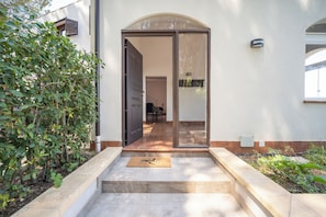 A house entrance with a glass door, a doormat, and a small garden area.