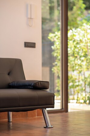 A modern room with a leather sofa, a wall-mounted phone, and a large window with a view of greenery.