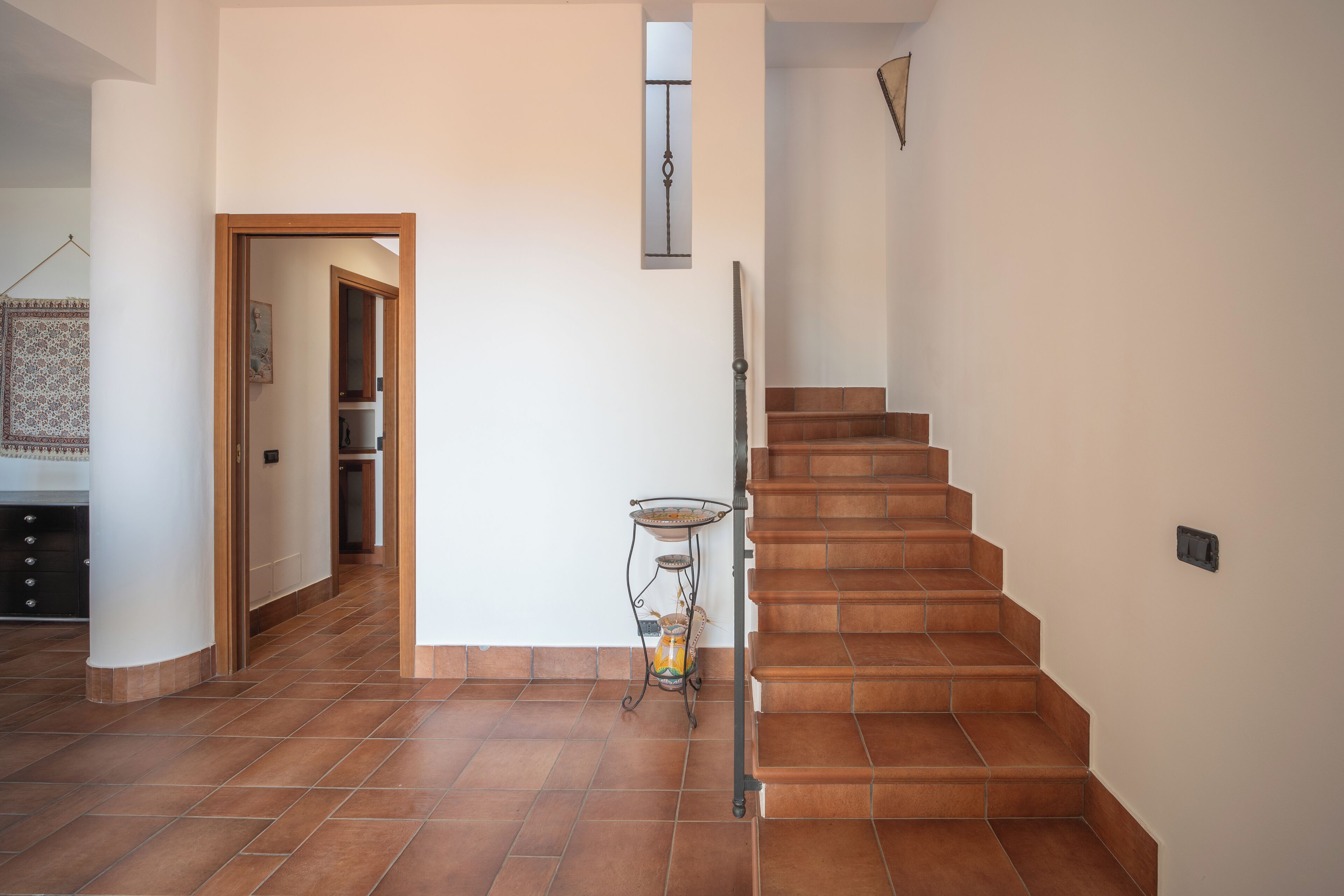 Un escalier avec une rampe métallique, un sol carrelé et une petite table sur laquelle est posé un vase.