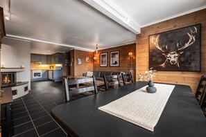 Ett modernt vardagsrum med en öppen spis, ett matbord och en stor tavla med ett rådjur på väggen.