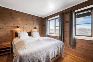 Ett sovrum med en väggpanel av trä, en stor säng, två sänglampor och ett fönster med gardiner.