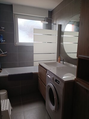 A compact bathroom with a washing machine, a bathtub, and a large mirror. - Cozy apartment with a balcony * Sleeps 4 * Near Strasbourg (Geispolsheim)