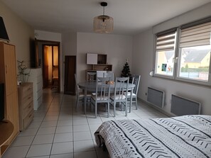 A bedroom with a bed, a dining area with chairs and a table, a small Christmas tree, and a window with blinds. - Cozy apartment with a balcony * Sleeps 4 * Near Strasbourg (Geispolsheim)