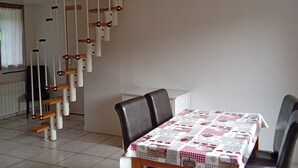 En matplats med ett bord dukat för fyra personer, en trappa med träräcken och en stol i bakgrunden.