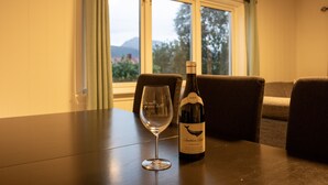 A table with a wine bottle and glass, a window with a view of trees and mountains, and a couch in the background. - Arctic Comfort 2, Tromsø (Tromsø)