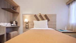 A hotel room with a bed, a nightstand, a lamp, a coffee maker, and a shelf with a kettle. - Amalia City Rooms (Chios)