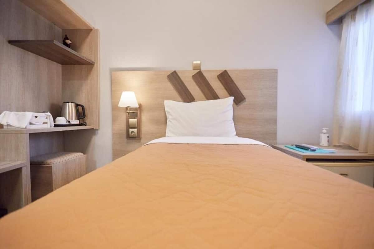 A hotel room with a bed, a nightstand, a lamp, a coffee maker, and a shelf with a kettle.