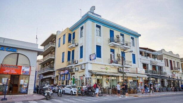 A street view with a building featuring balconies, a travel shop, and parked motorcycles. - Amalia City Rooms (Chios)