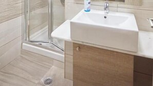 A bathroom with a glass shower enclosure, a white sink, and a mirror. - Amalia City Rooms (Chios)