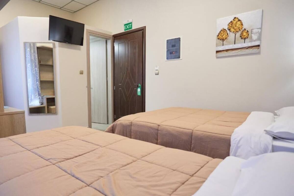 A hotel room with two beds, a TV mounted on the wall, an exit sign, and a painting.
