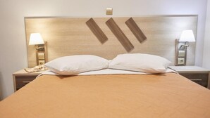 A hotel room with a large bed, two bedside lamps, a nightstand with a phone, and a wall-mounted light switch. - Amalia City Rooms (Chios)