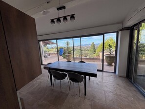 A modern dining area with a large table and chairs, large windows with a view of a cityscape and mountains, and a ceiling with pendant lights. - 550-square-meter vacation rental home in Mougins (Mougins)
