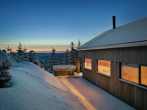 A wooden cabin with large windows, surrounded by snow-covered trees and a view of the landscape. - Mountain cabin near Hafjell with view and hot tub (Øyer)