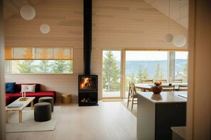 A modern interior with a fireplace, a sofa, a dining area, and large windows offering a view. - Mountain cabin near Hafjell with view and hot tub (Øyer)