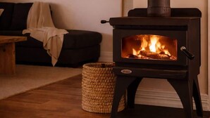 A wood-burning stove with a fire, a sofa, and a woven basket in a living room. - Cosy Retreat w/ Sauna & Fire Pit | Golf & Beach (preston beach)