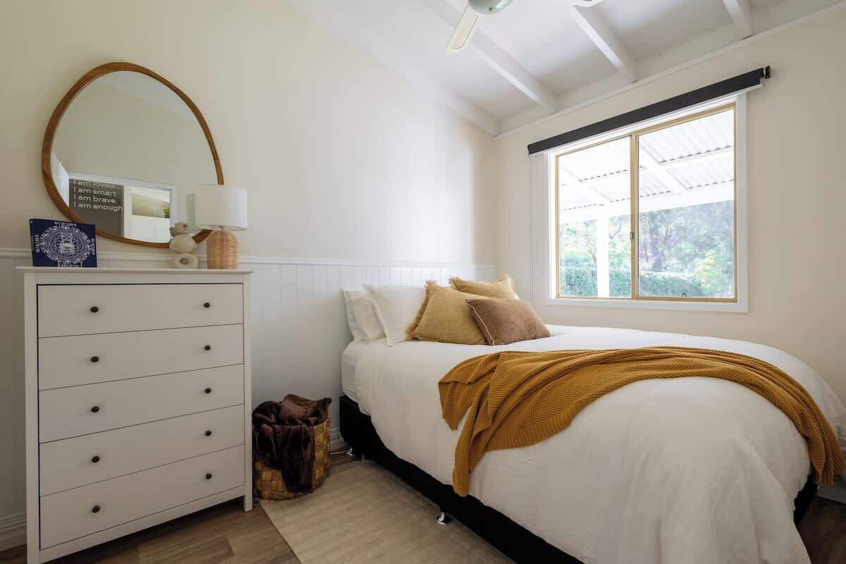 A bedroom with a bed, dresser, mirror, and window.