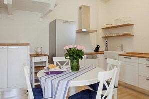 Eine moderne Küche mit weißen Schränken, einem Edelstahl-Kühlschrank, einer Holz Arbeitsplatte und einem Essbereich mit einer Streifen Tischdecke und weißen Stühlen.