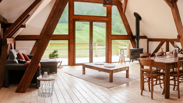 A spacious loft with a large window, wooden beams, a dining table, and a fireplace.