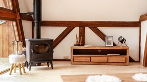 Ein gemütlicher Raum mit Kaminofen, einer Holzbank und einem flauschigen Hocker.