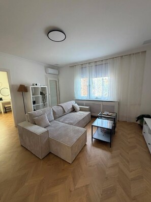 A modern living room with a sectional sofa, a glass coffee table, and a large window with sheer curtains. - Spacious Apartment Near Vienna Schwechat Airport I Parking & 2 Bedrooms (Schwechat)