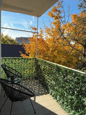 A covered outdoor area with a tiled floor, two black chairs, and a green leafy wall. - Spacious Apartment Near Vienna Schwechat Airport I Parking & 2 Bedrooms (Schwechat)